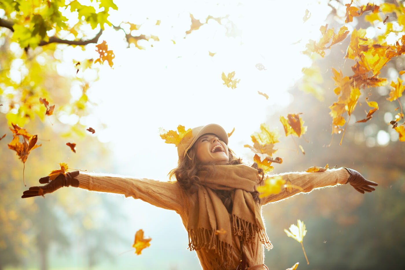 Woman laughing with arms wide open as golden autumn leaves fall around her